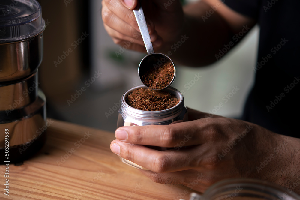 Barista holding moka pot with ground coffee in coffee shop.