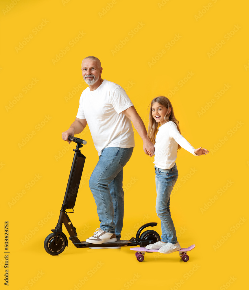 Little girl and her grandfather with electric scooter and skateboard on yellow background