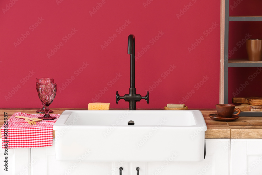 Counter with modern sink and clean dishware near color wall