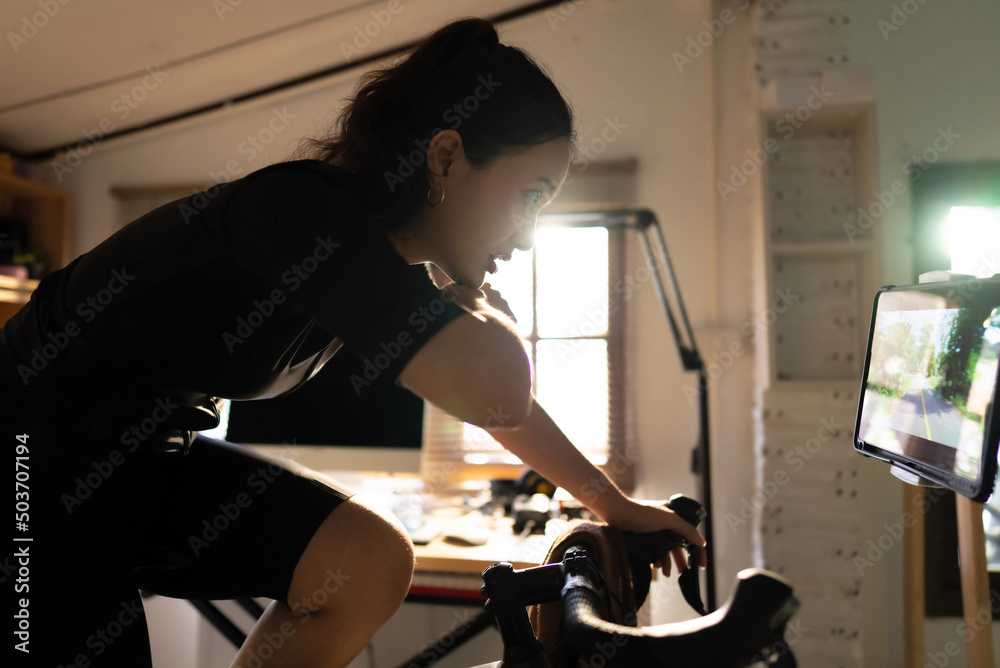 Female Asian cyclist, She is exercising at home. She rides a bike simulator.