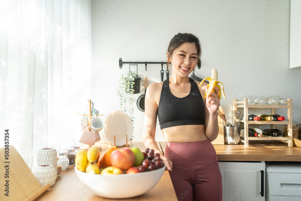 亚洲有魅力的活跃运动女性在家里的厨房里拿着香蕉。