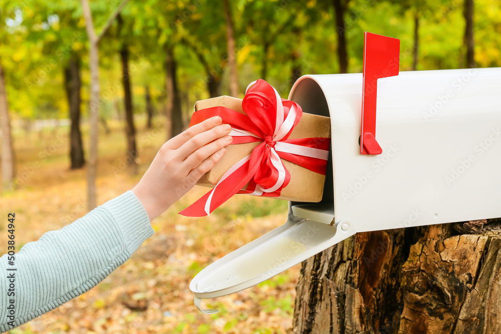 Woman putting gift into mailbox in autumn park