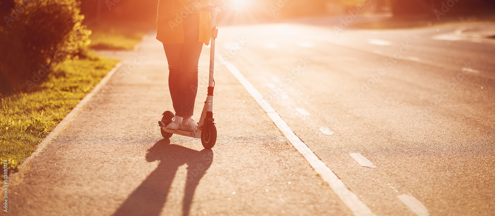 Woman riding on scooter on asphalt road in summer