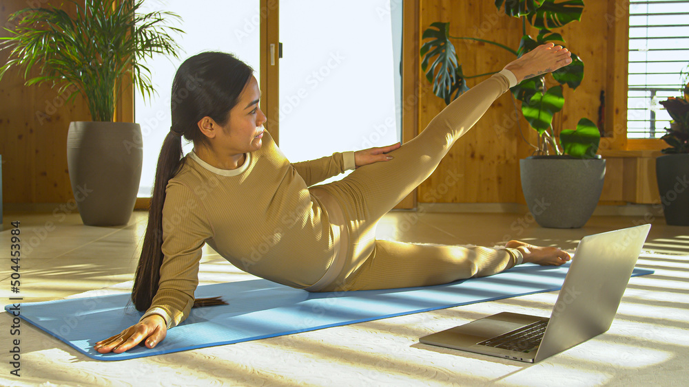 特写：一位运动型亚洲女性带着笔记本电脑参加在线普拉提锻炼班