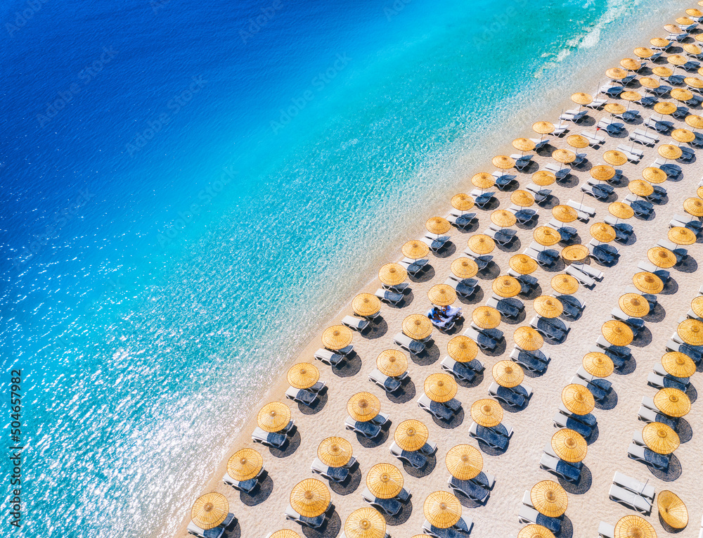 Aerial view of blue sea, empty sandy beach with sun beds and umbrellas at sunset in summer. Blue lag