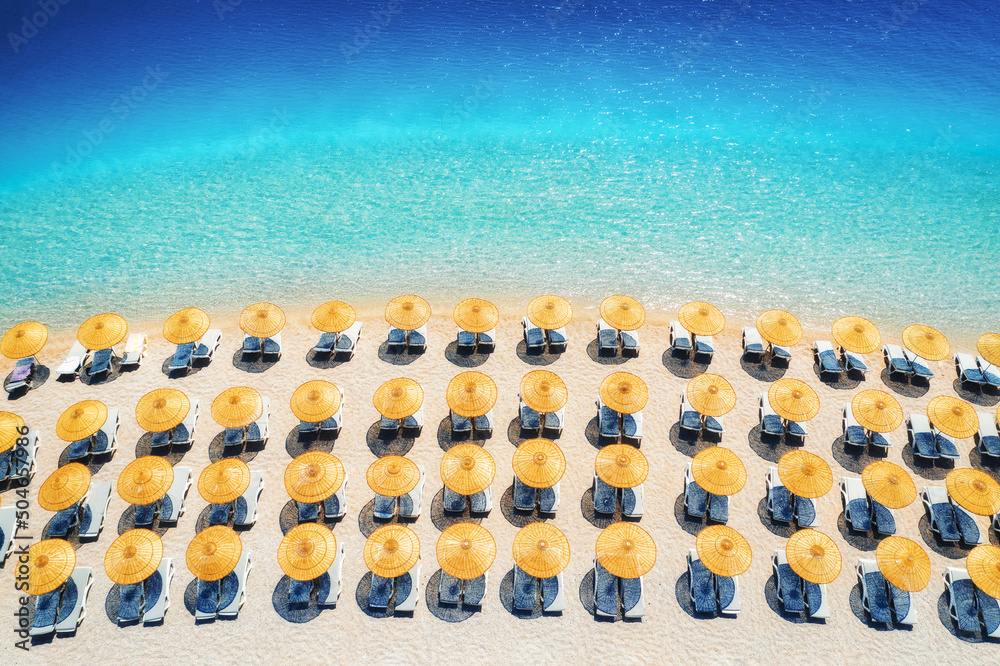 Aerial view of blue sea, empty sandy beach with sun beds and umbrellas at sunrise in summer. Blue la