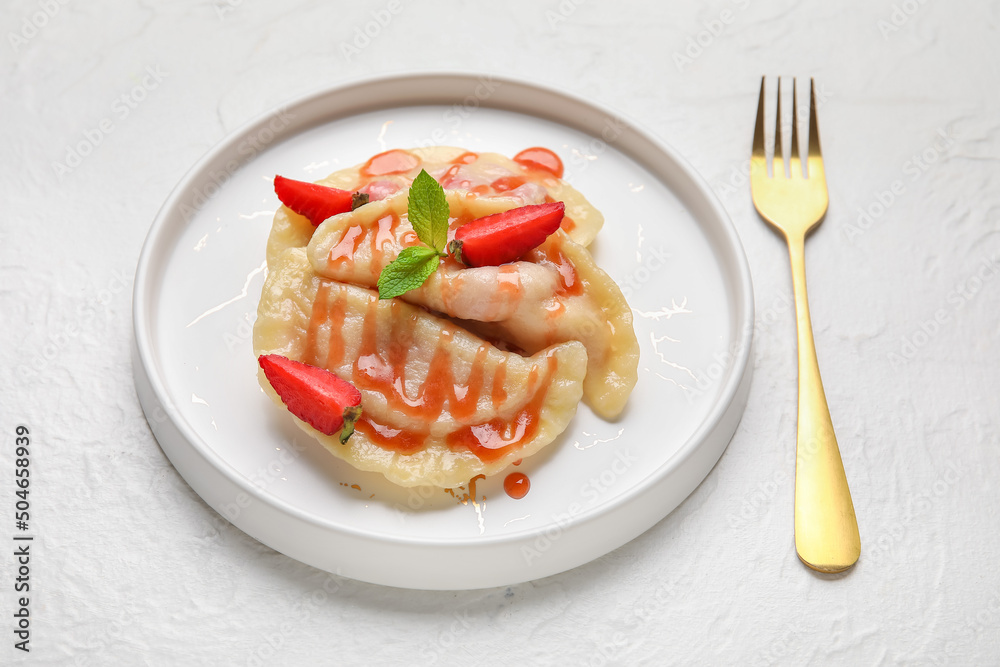 Plate with strawberry dumplings and sweet sauce on light background