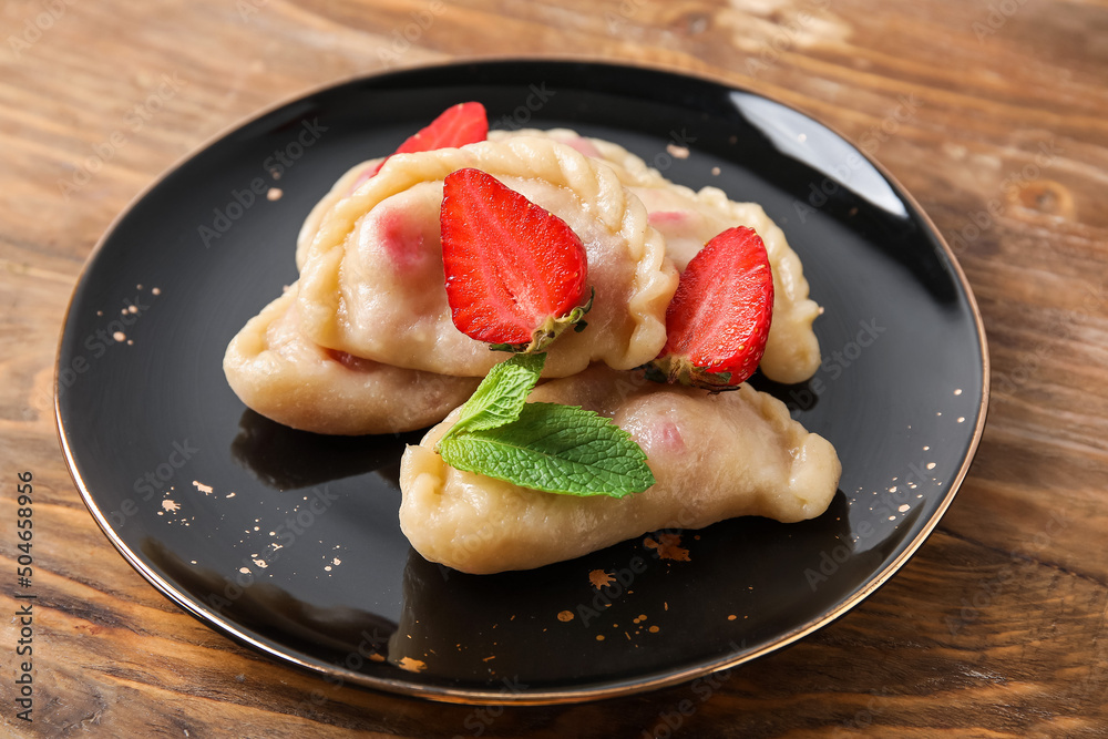 Plate with sweet strawberry dumplings on wooden background, closeup