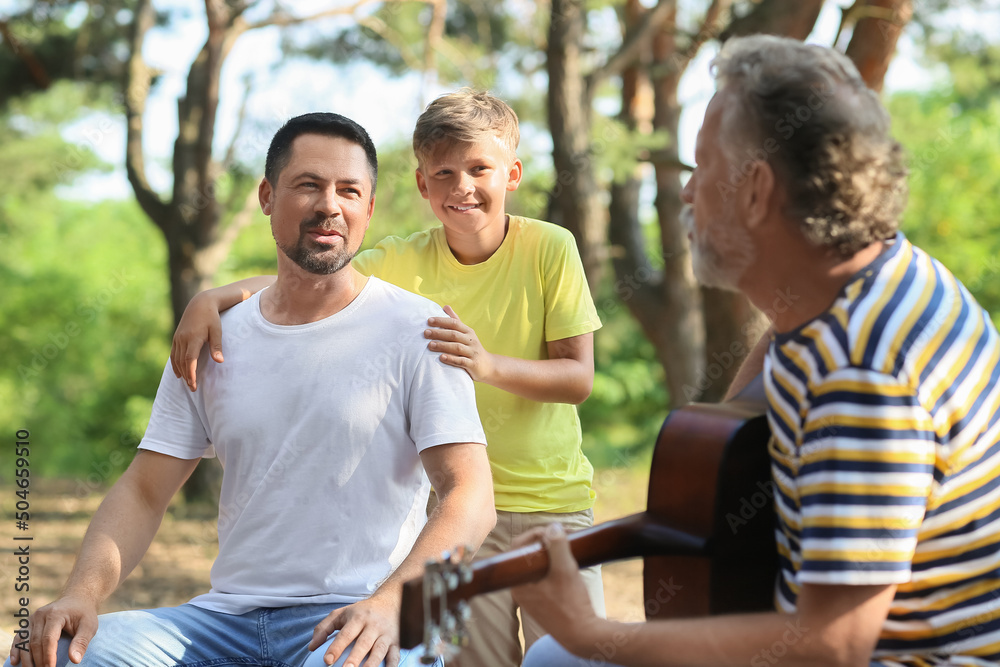 Senior man playing guitar for his son and little grandson in forest