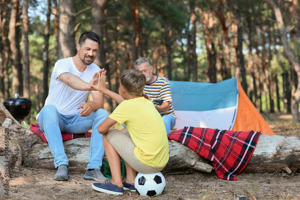 Handsome man giving high-five to his little son in forest