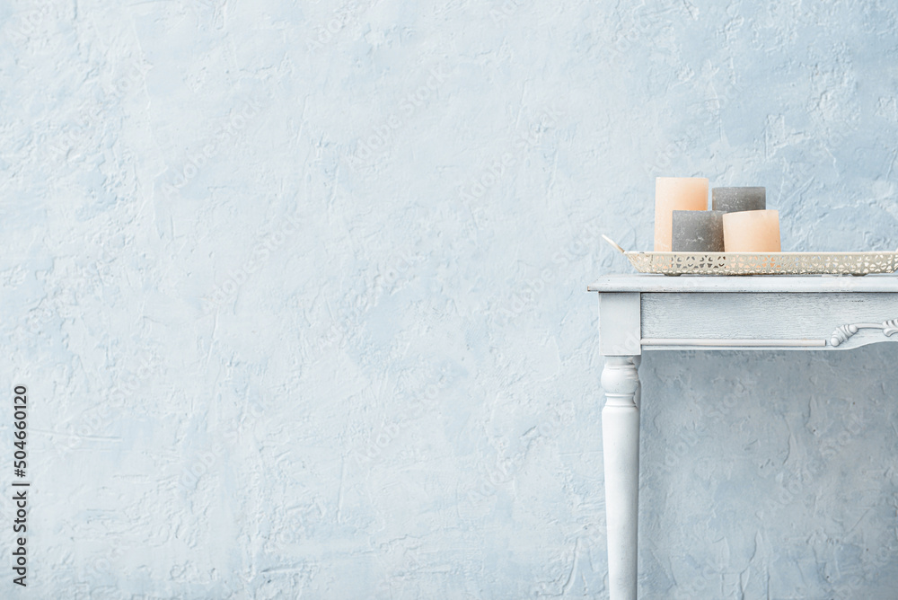 Tray with candles on wooden table near color wall