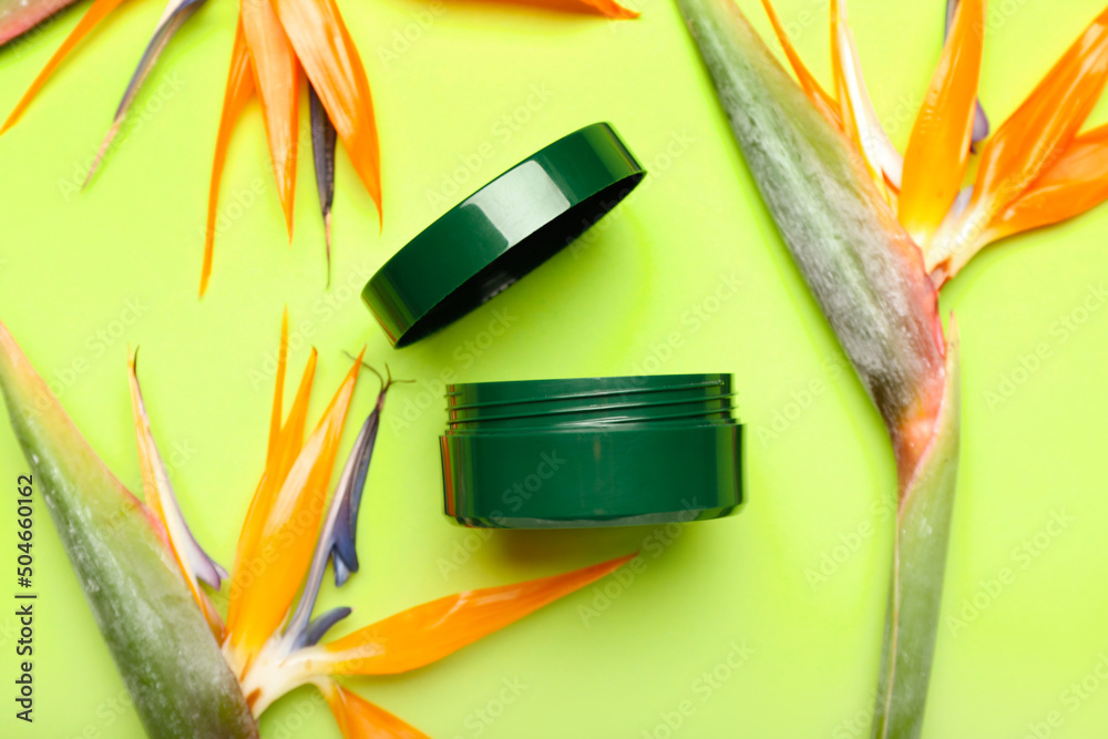 Jar of cosmetic product and strelitzia flowers on green background