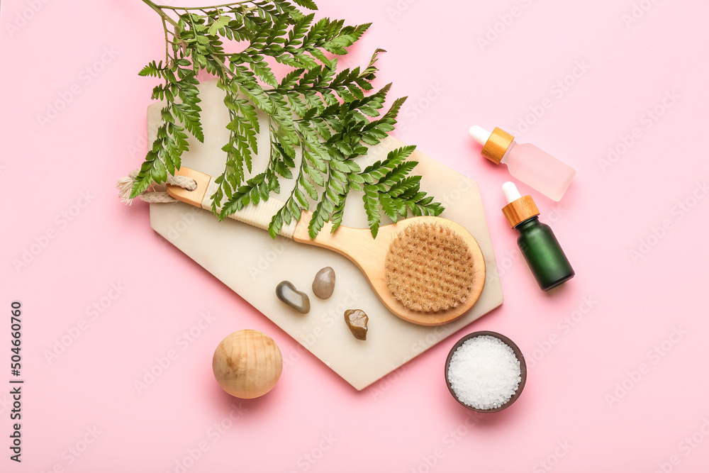 Composition with bottles of essential oil, sea salt and massage brush on pink background