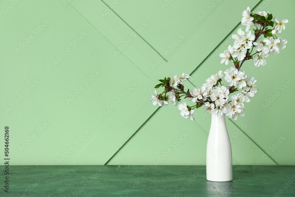 White vase with beautiful blooming branches on table near green wall