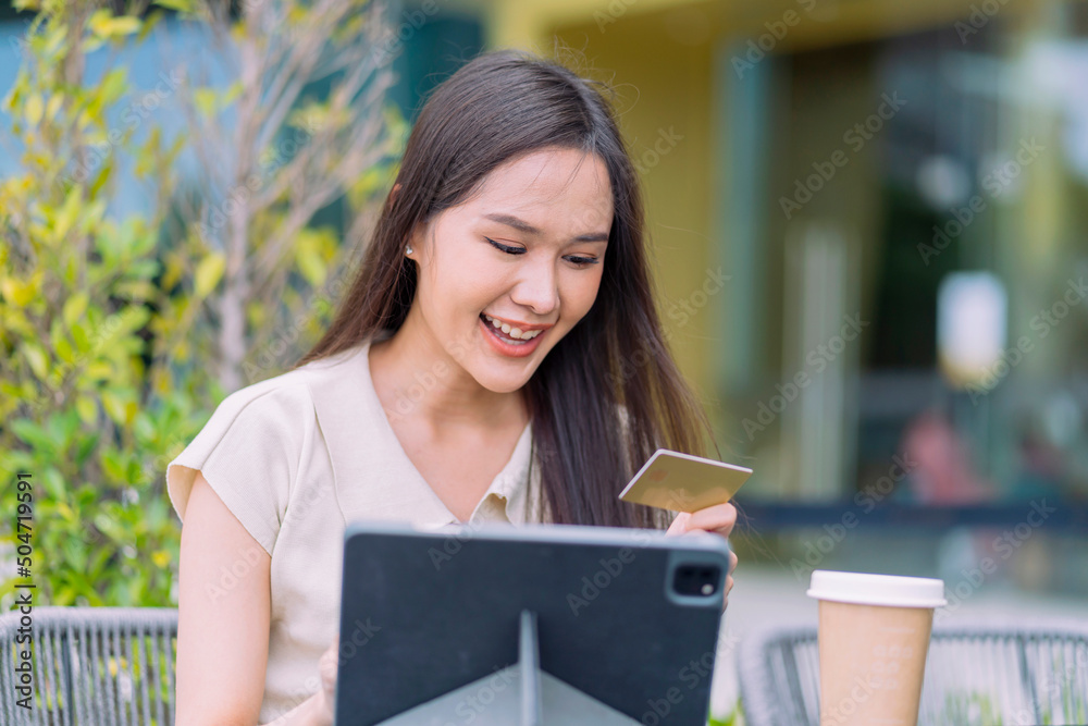 亚洲女性在网上购物并用信用卡付款。女性坐在户外咖啡馆享受