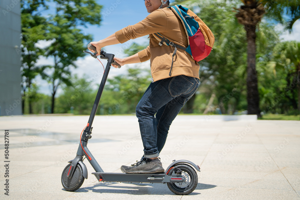 An Asian man rides an electric scooter to work.