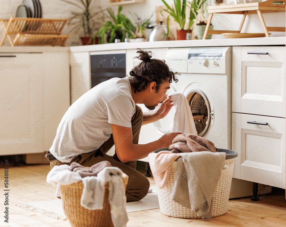 Young african american male householder loading washing machine