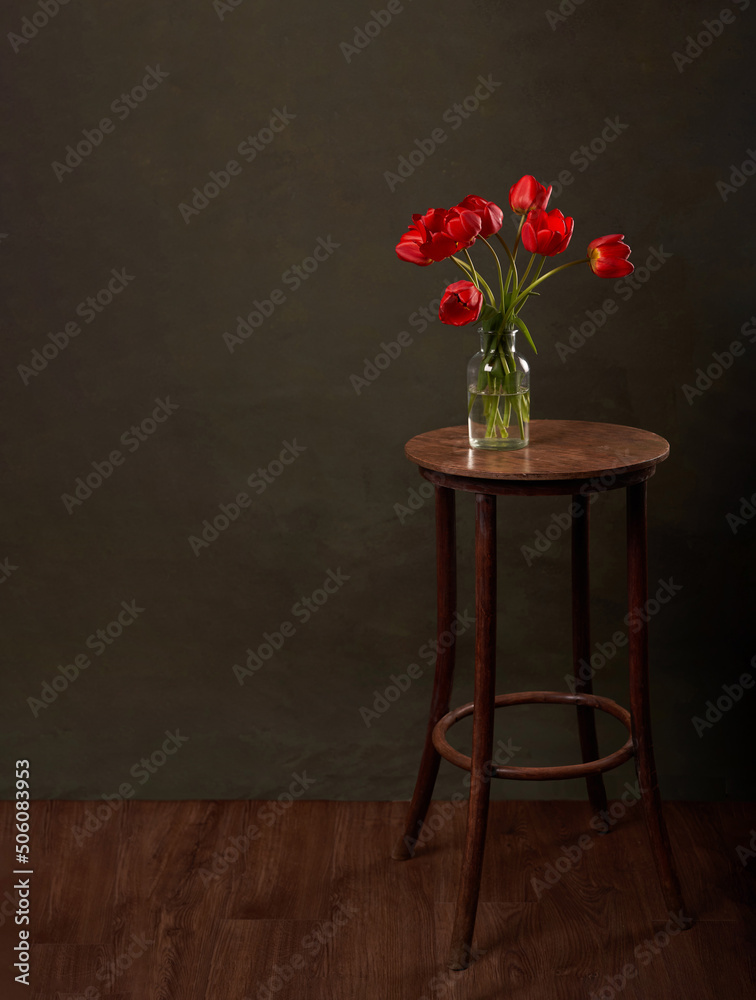 Vase with flowers on vintage table. Round table with red tulips on dark green background with copy s