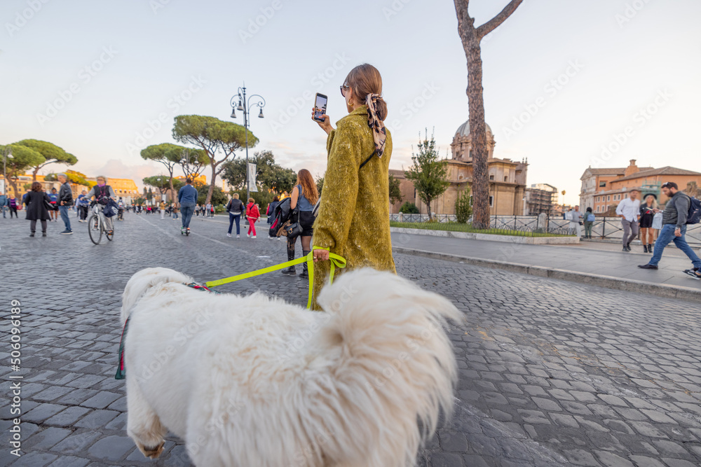 Woman walking with a dog on the famous central street in Rome, taking photos on phone and enjoying o