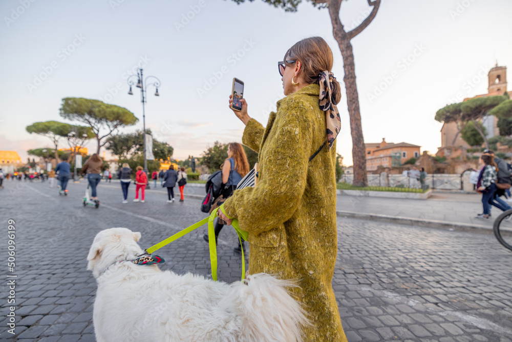 Woman walking with a dog on the famous central street in Rome, taking photos on phone and enjoying o