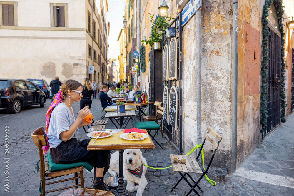 Woman sitting at traditional restaurant on the beautiful cozy street in Rome. Concept of Italian gas