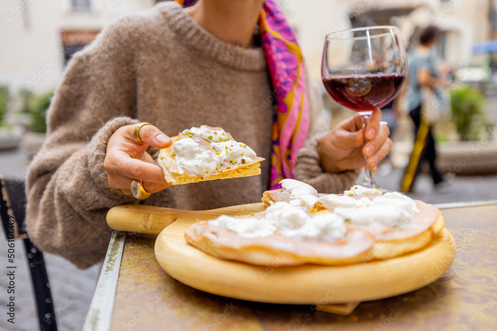 Woman holding pizza and a glass of wine at outdoor restaurant. Concept of Italian gastronomy and tra