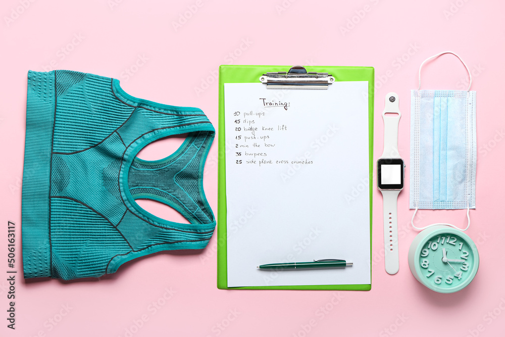 Clipboard with training, sport top, medical mask and smartwatch on pink background