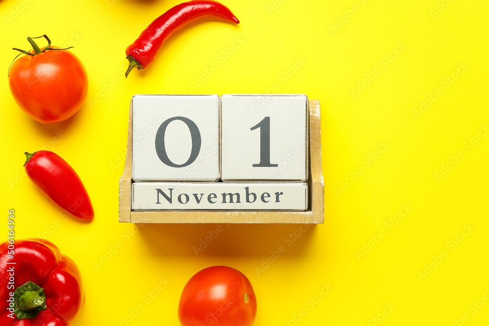 Wooden cube calendar with date NOVEMBER 1 and vegetables on yellow background, closeup. World Vegan 