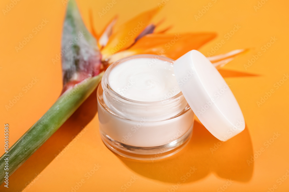 Jar of cream and strelitzia flowers on color background, closeup