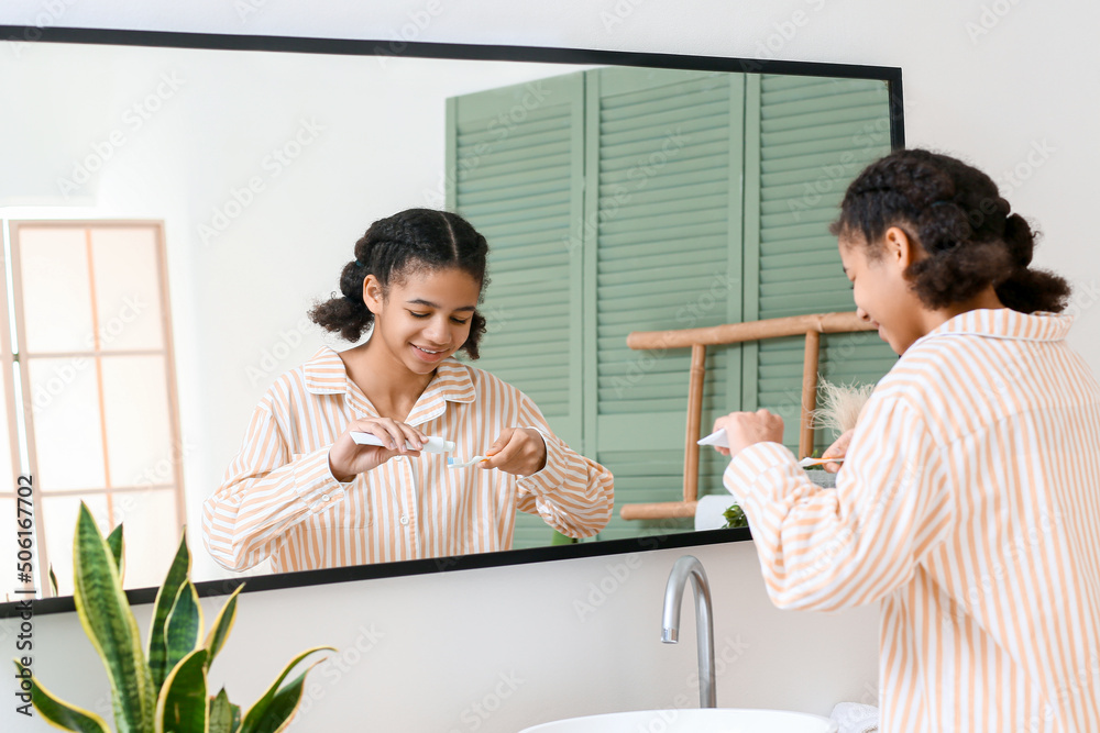 African-American teenage girl applying tooth paste onto brush in bathroom