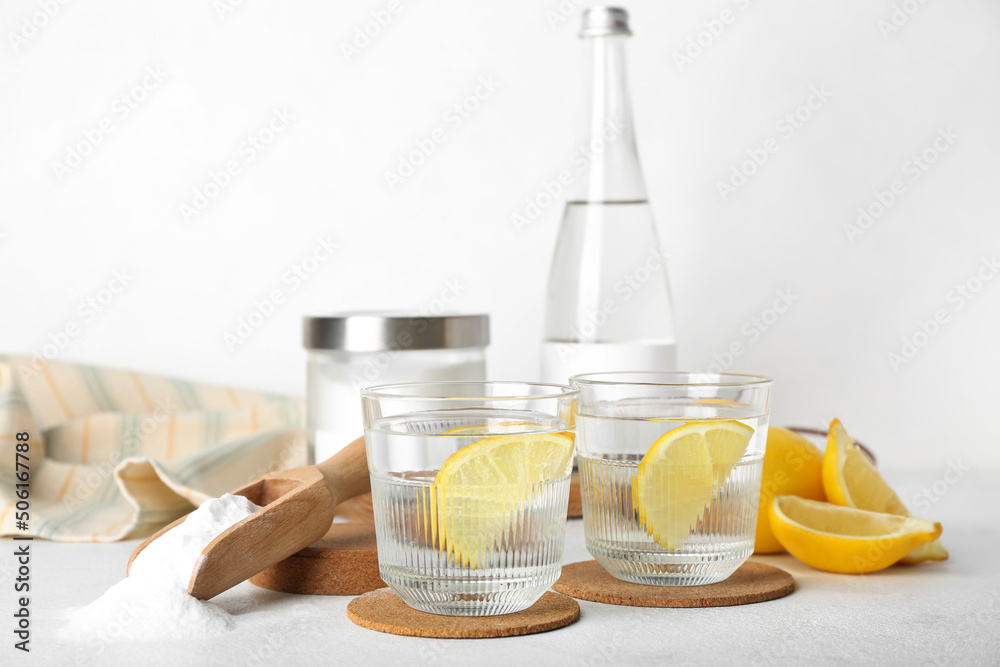 Scoop with baking soda, glasses of water and lemons on light background