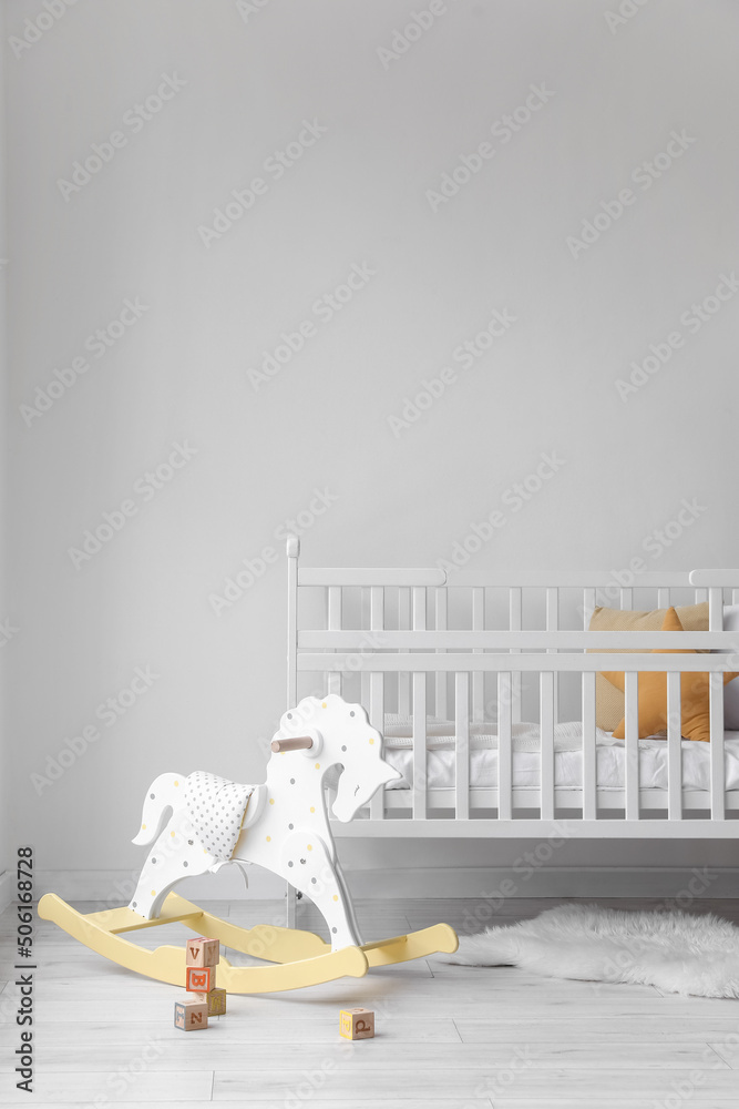 Baby crib and rocking horse with cubes near light wall