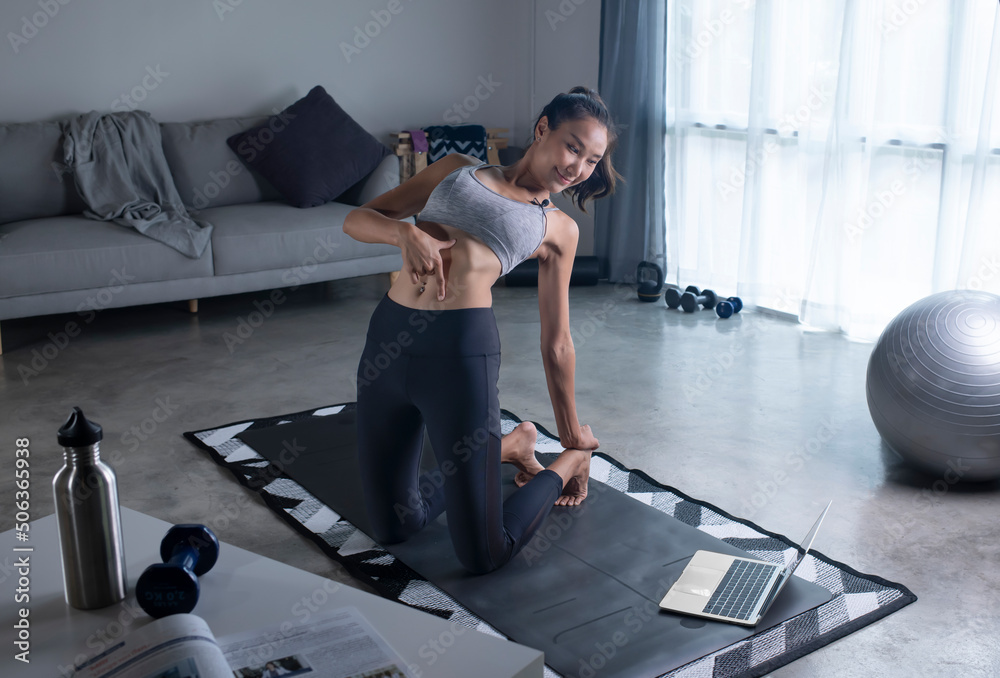 Sporty young Asian woman in sportswear exercising at home, watching fitness video on Internet or hav