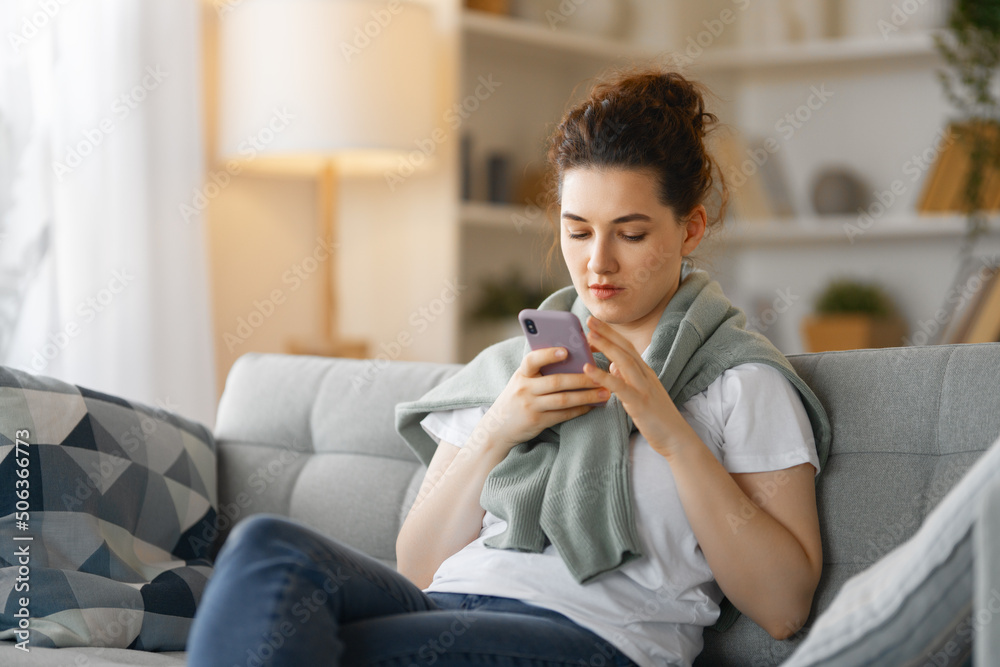 woman is using a phone sitting on a sofa