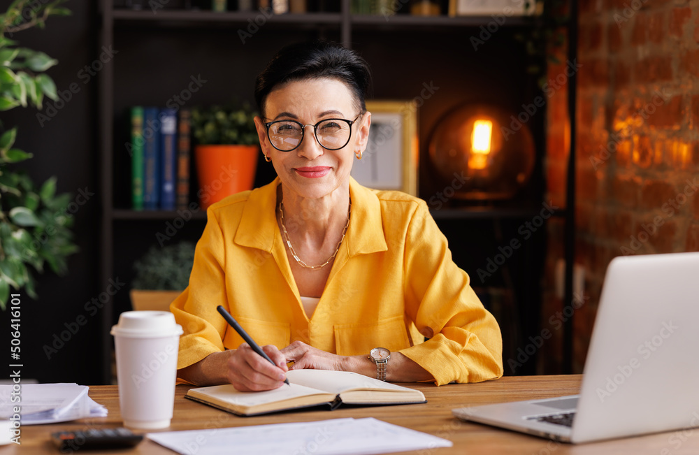 Middle aged businesswoman working at laptop,   take notes in home office