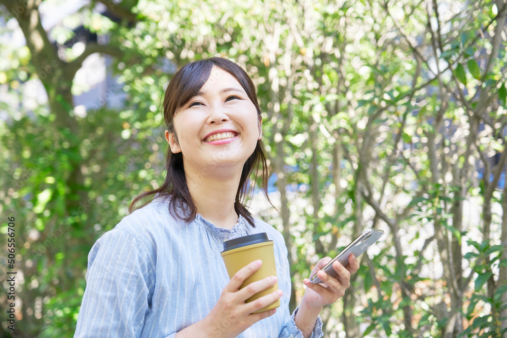 屋外でスマホを持ってコーヒーを飲む女性