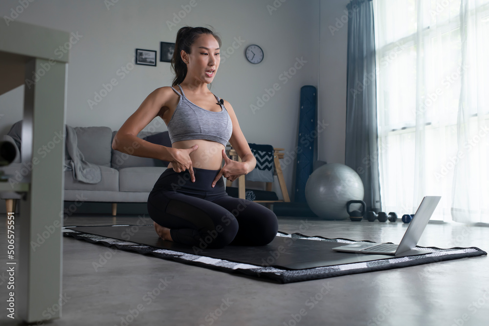 Sporty young Asian woman doing yoga in front of laptop in living room, young female in sportswear ex