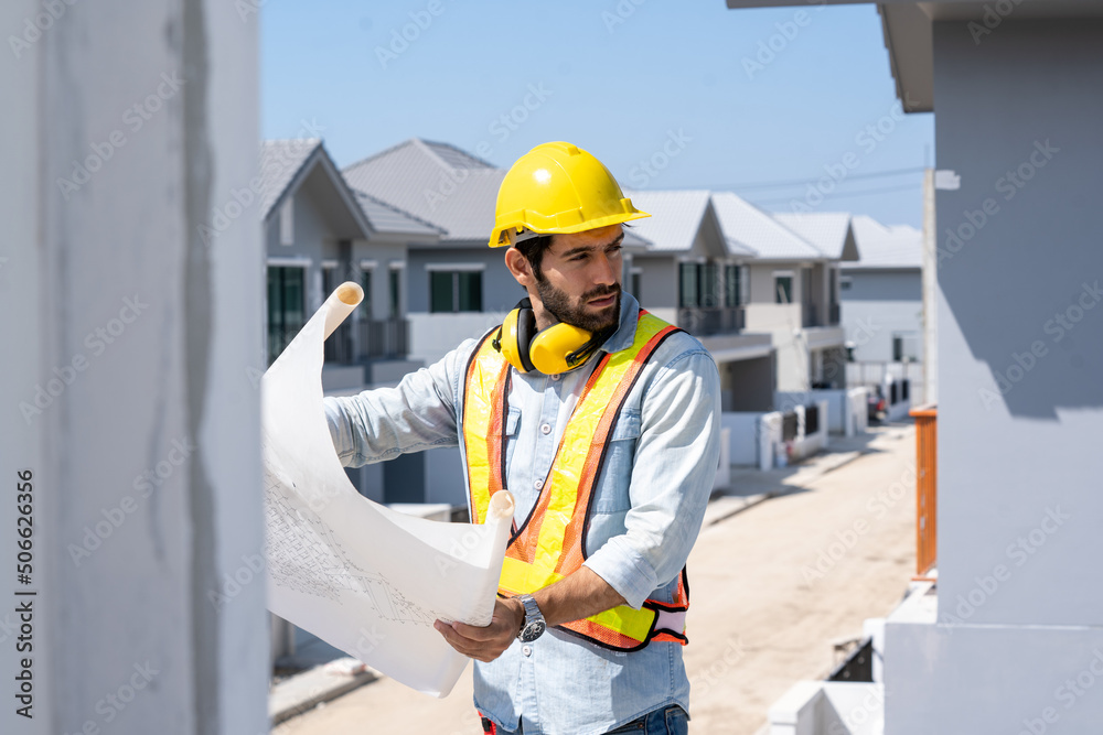 Architect in yellow helmets reviewing blueprints at a construction site.