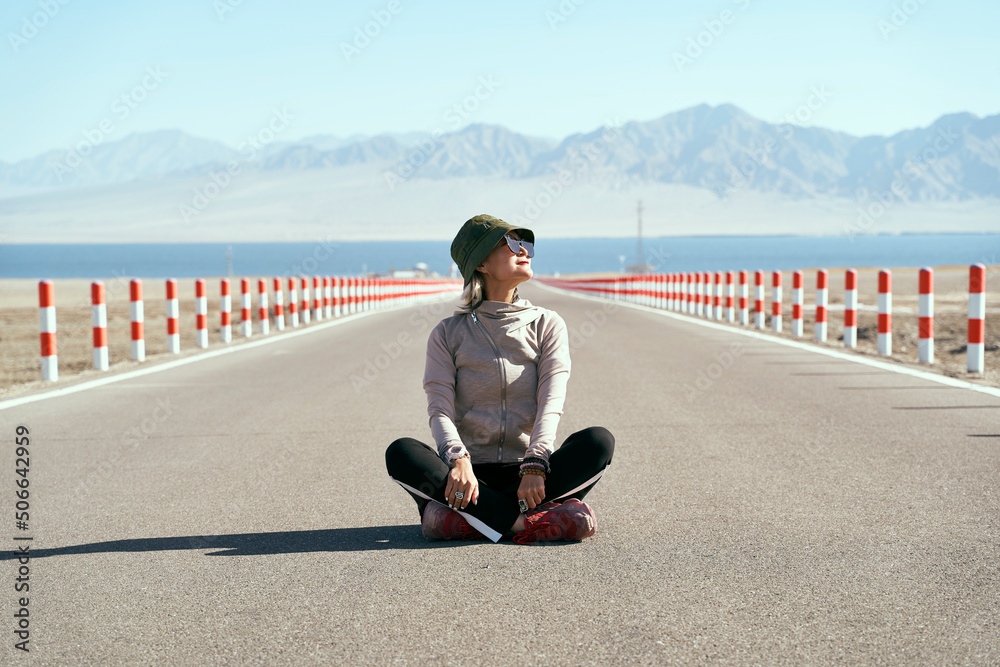 asian woman tourist sitting in the middle of empty road looking at view