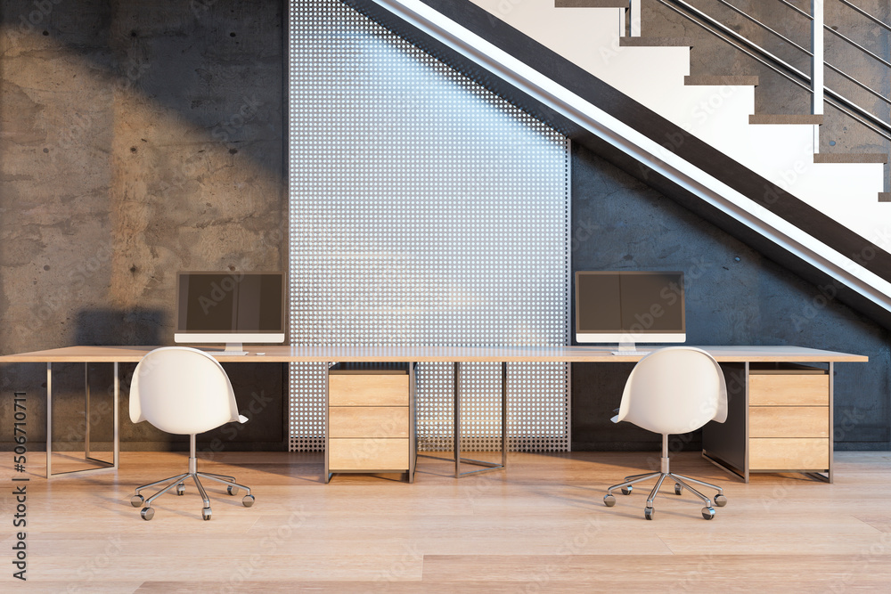 Front view on stylish work places with modern computers, perforated metal and concrete wall, part of