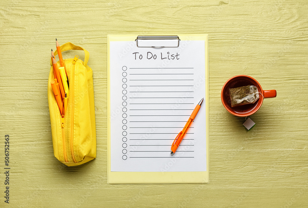 Clipboard with blank to do list, pencil case and cup of tea on color wooden background