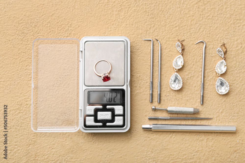 Jewelry scales with ring, earrings and different tools on beige background