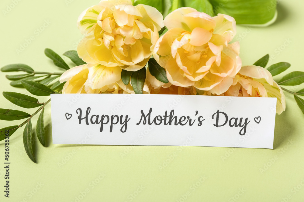 Paper with text HAPPY MOTHERS DAY and flowers on green background, closeup