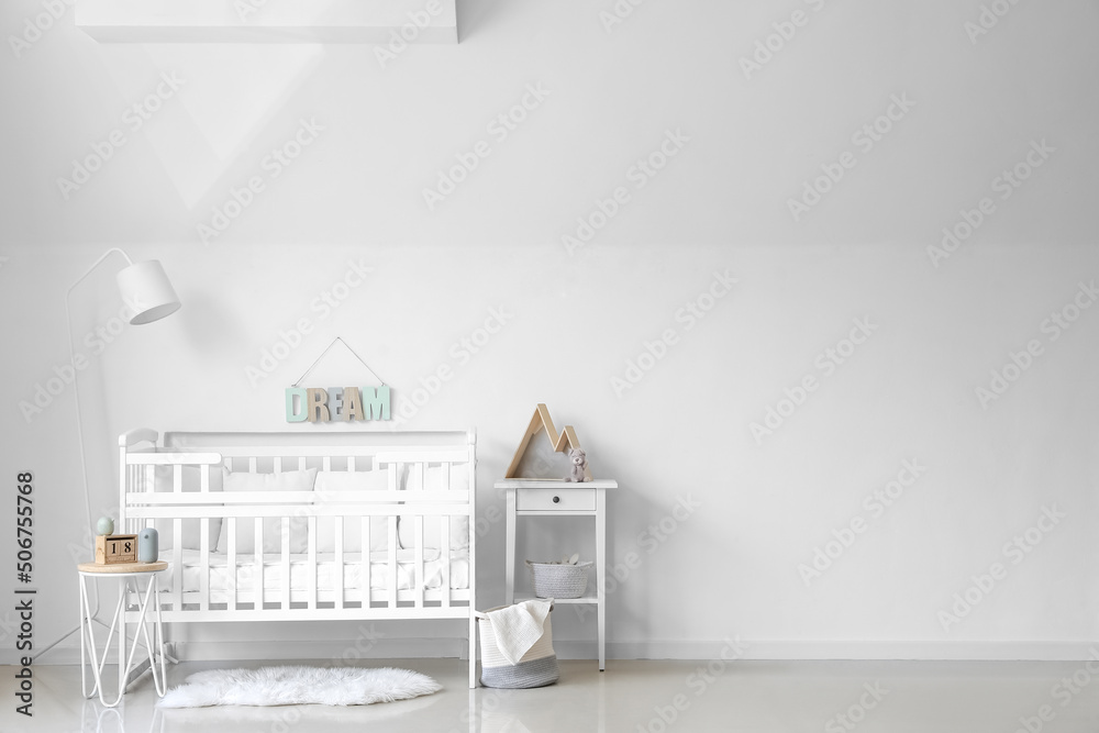 Interior of light nursery with baby crib, lamp and tables