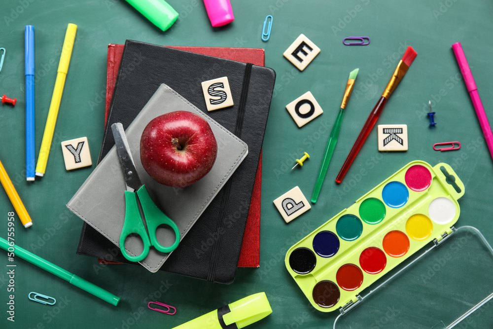 School stationery with paints and apple on green chalkboard