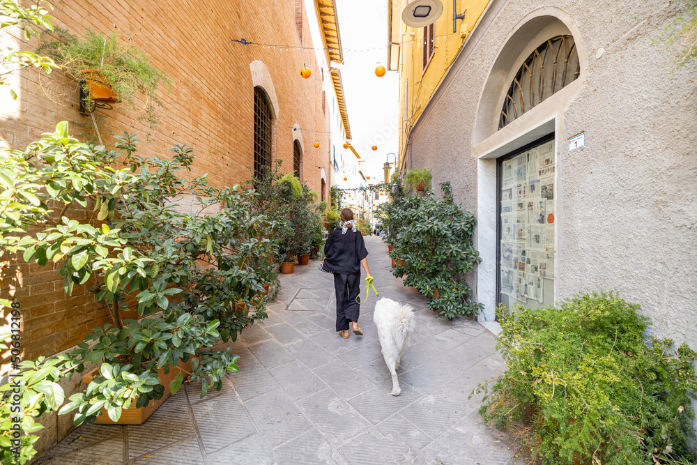 Woman walking with dog on narrow street in the old town of Grosseto, in Maremma region of Italy. Mar