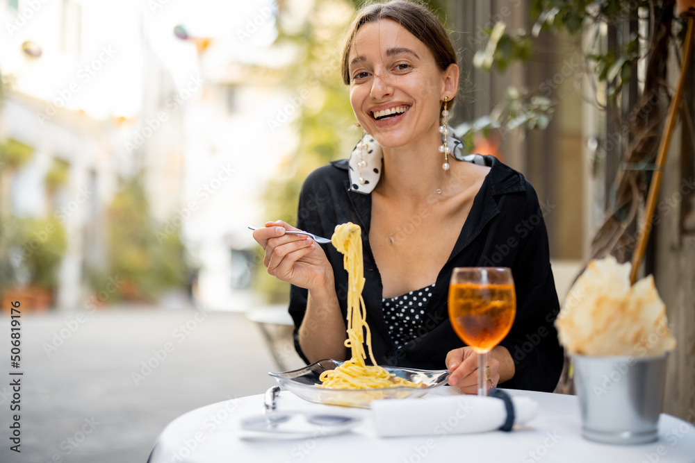 一个微笑的女人在户外舒适的意大利餐厅吃意大利面和葡萄酒的肖像。它的概念