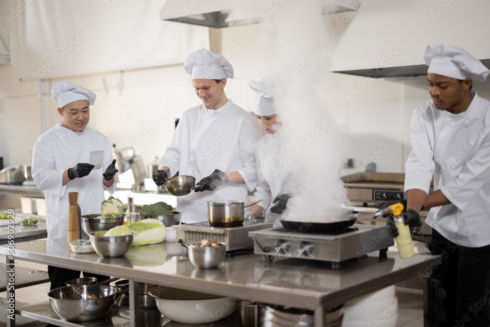 Multiracial team of professional cooks in uniform preparing meals for a restaurant in the kitchen. L