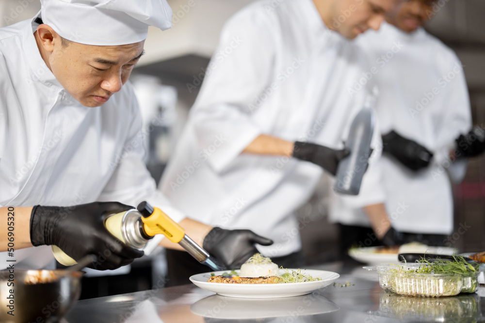 Multiracial group of cooks finishing main courses while working together in the kitchen. Asian chef 