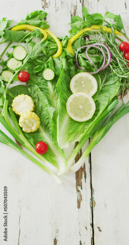 Vertical image of fresh tomatoes and green vegetables forming heart on white rustic background